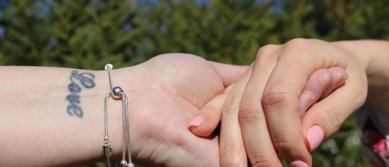 Two females holding hands, tattood wrist, nature background