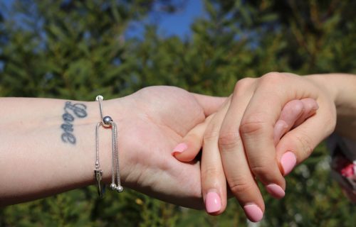 Two females holding hands, tattood wrist, nature background