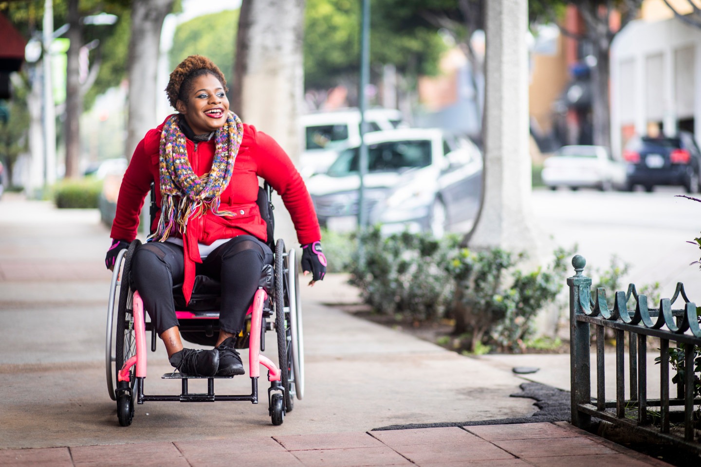 A young black disabled woman with a wheelchair and a bright colored sweater and her Asian friend walk around the city.