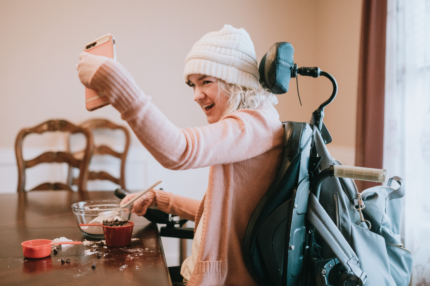 An independent young adult woman with cerebral palsy going about some of her daily routines at home. She smiles for a self portrait with her smartphone while mixing together ingredients for making chocolate cookies.